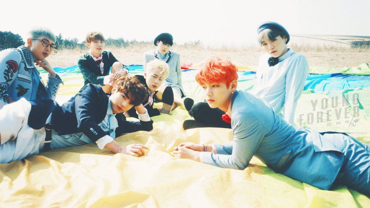 BTS üyeleri yaz aylarında sahilde bir örtü üzerinde uzanırken.
