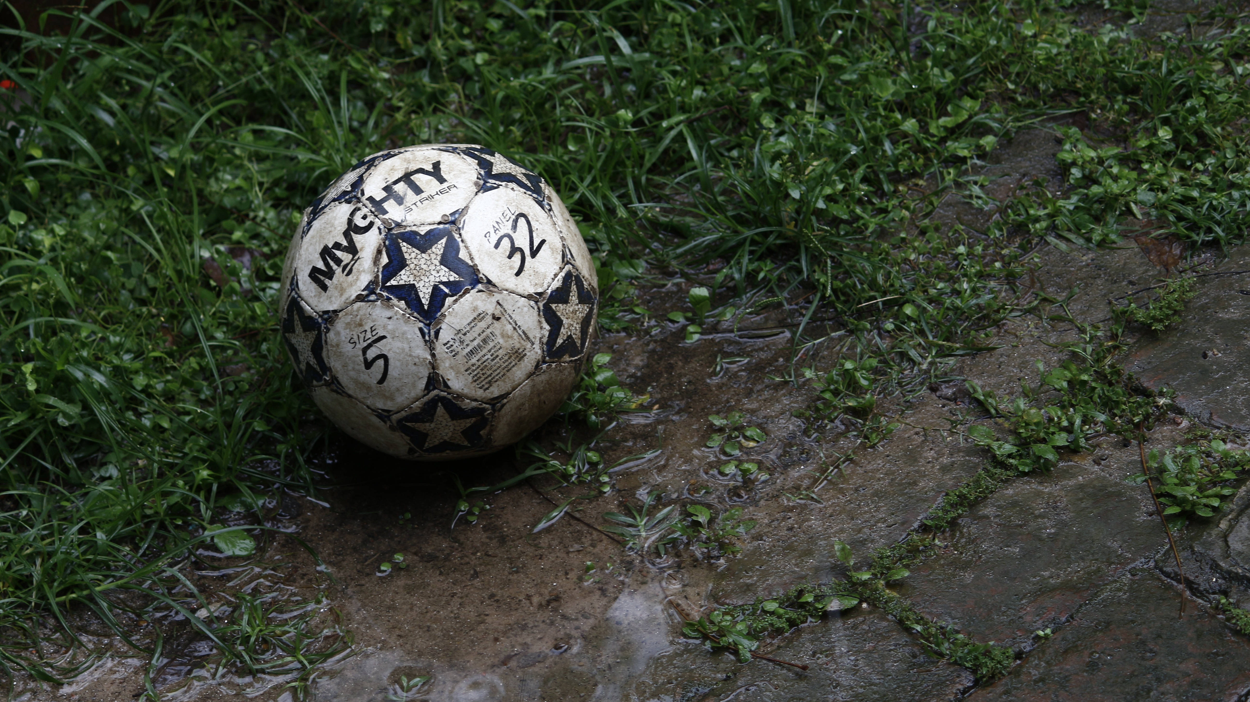 Çamurlu bir futbol topu çimenlerde sahipsiz yatıyor. Duvar Kağıdı