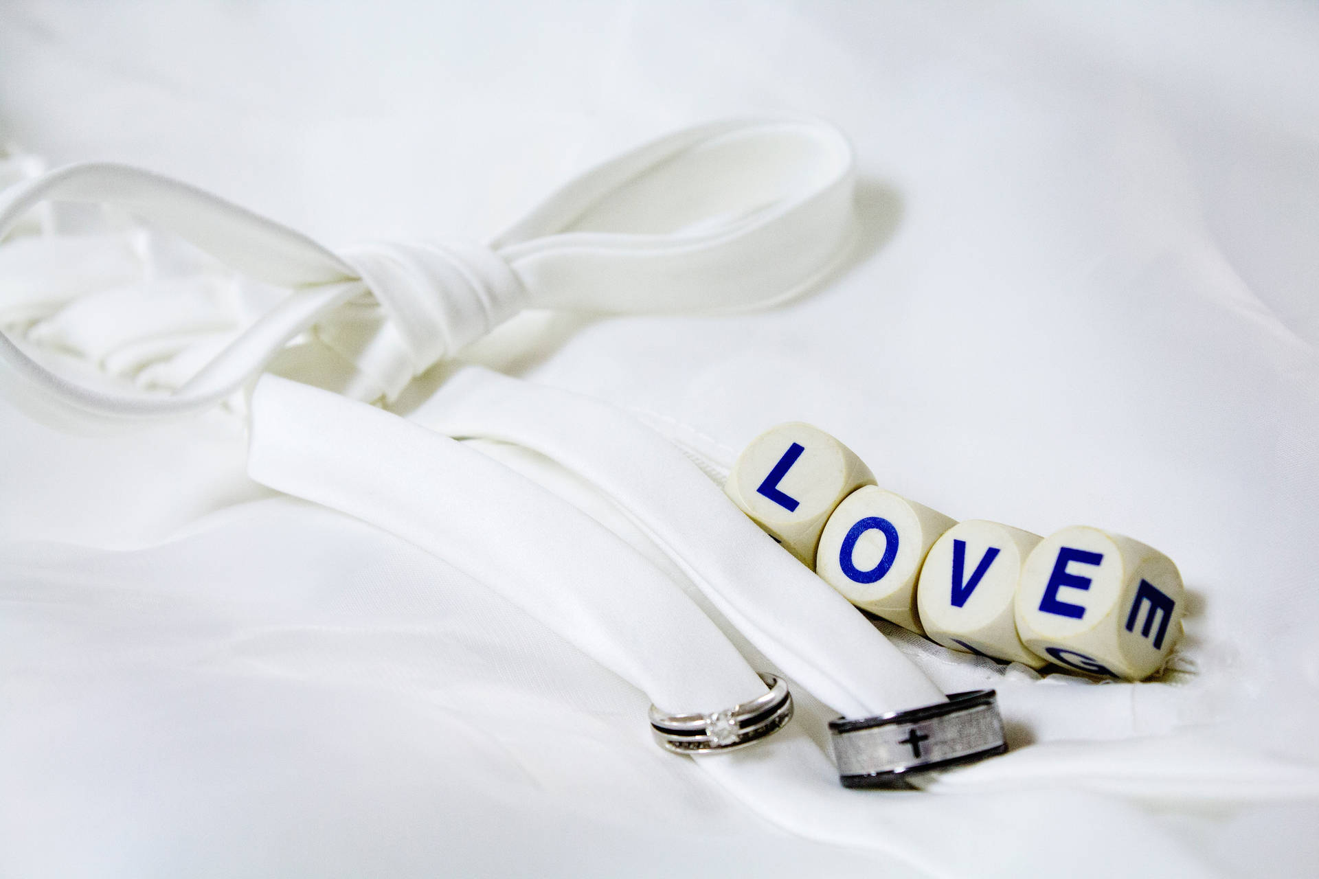 Beyaz bir örtü üzerinde gümüş ve siyah iki düğün yüzüğünün yanında, beyaz bir kurdele ile bağlanmış dört zar üzerinde 'Love' yazısı.