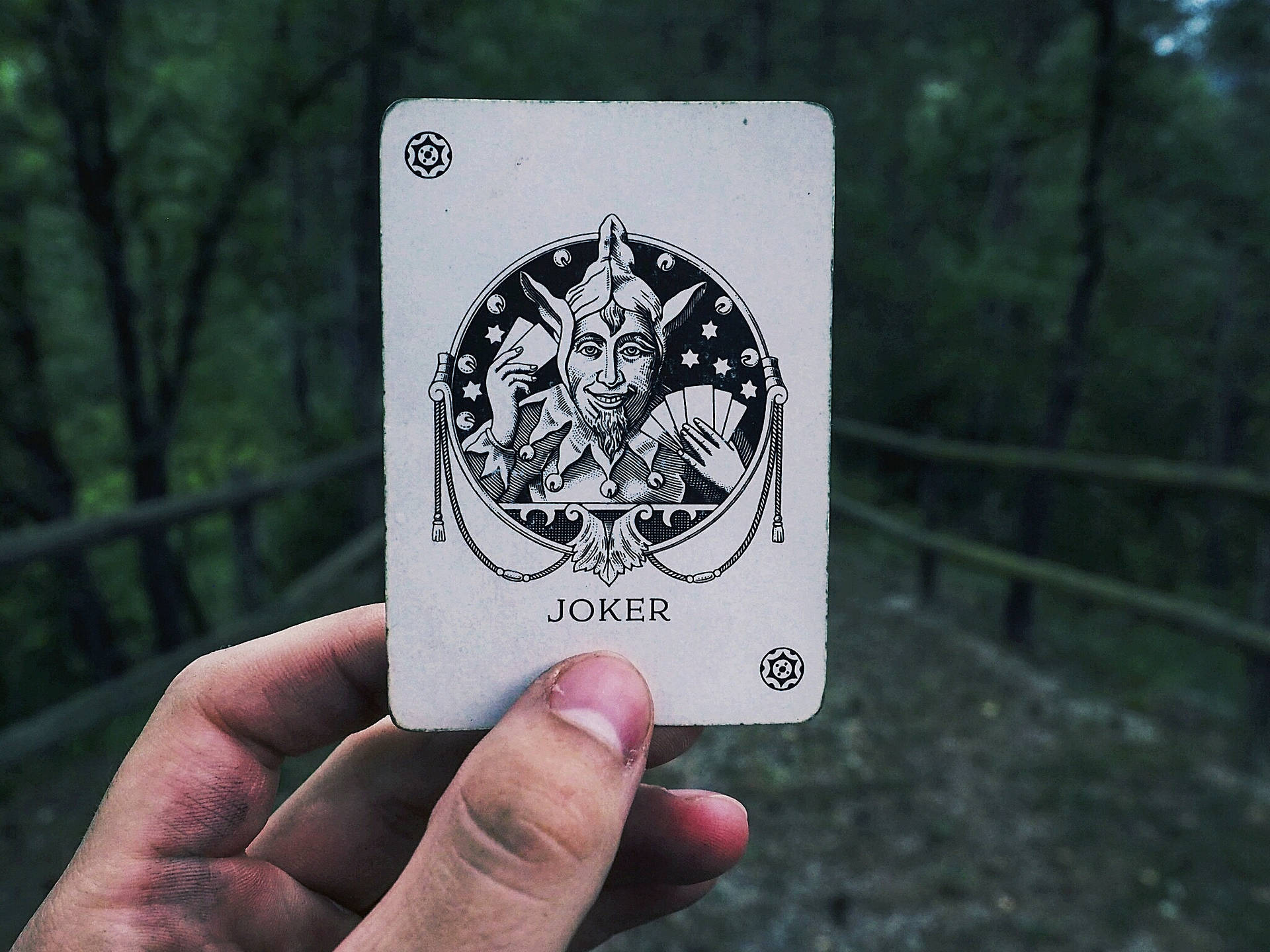 Bulanık bir köy yolu arka planında joker kartı tutan el.