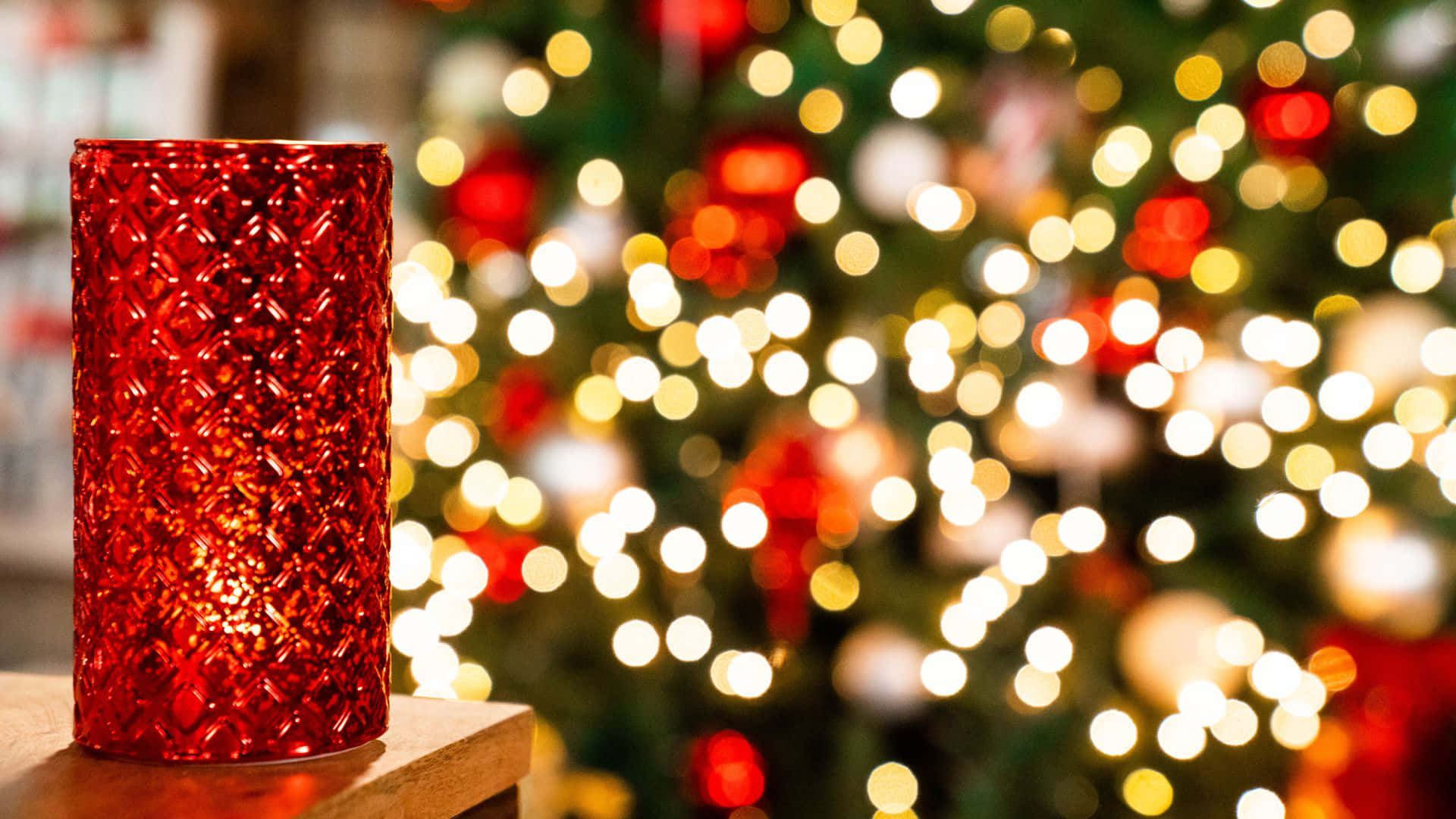 Kırmızı bir mum, bir Noel ağacının önündeki masanın üzerinde duruyor Duvar Kağıdı