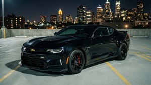 Siyah bir Camaro ZL1, gece şehir siluetiyle birlikte bir çatı katı otoparkında duruyor.