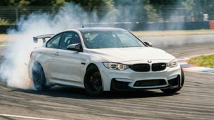 Beyaz bir BMW M4, yarış pistinde bir virajı dönerken lastik dumanı ve hareket bulanıklığı ile drift yapıyor. — BMW Duvar Kağıdı