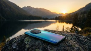 Huawei telefon, gün batımında bir dağ gölüne bakan bir kayanın üzerinde, huzurlu manzara.