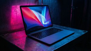 Karanlık bir odada neon yansımaları olan siberpunk esintili bir MacBook.